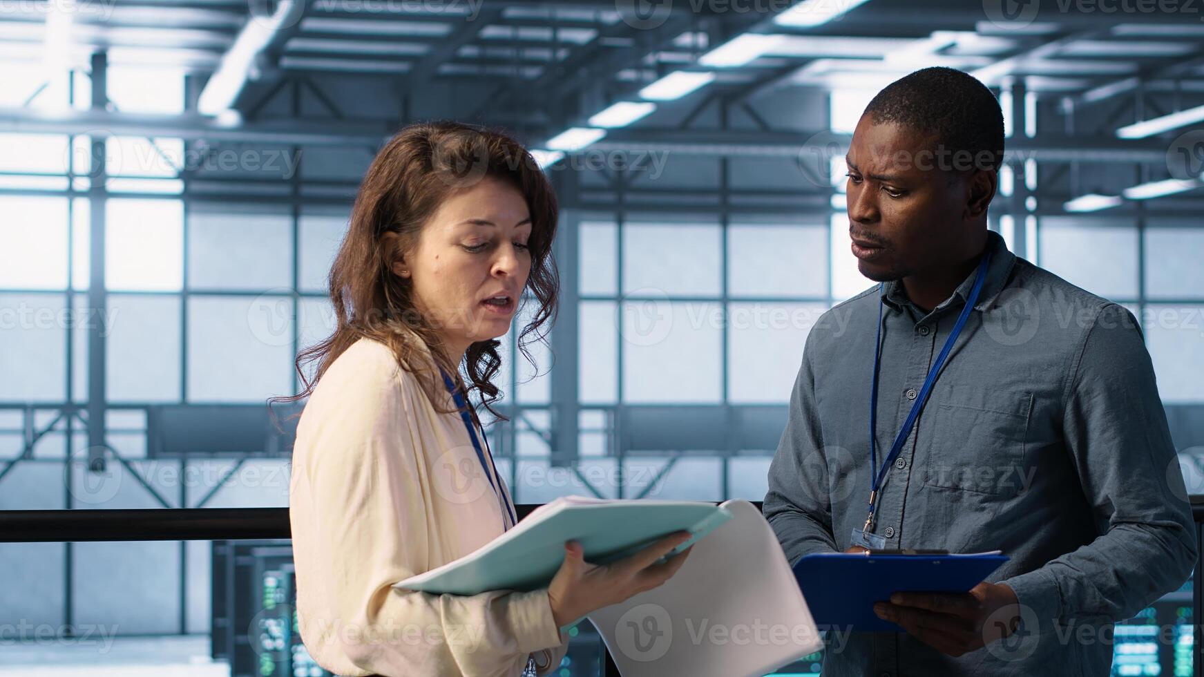 Cheerful admins meeting in data center to review reports and files. Server room employee handshaking colleague, doing troubleshooting to prevent downtime, camera A photo