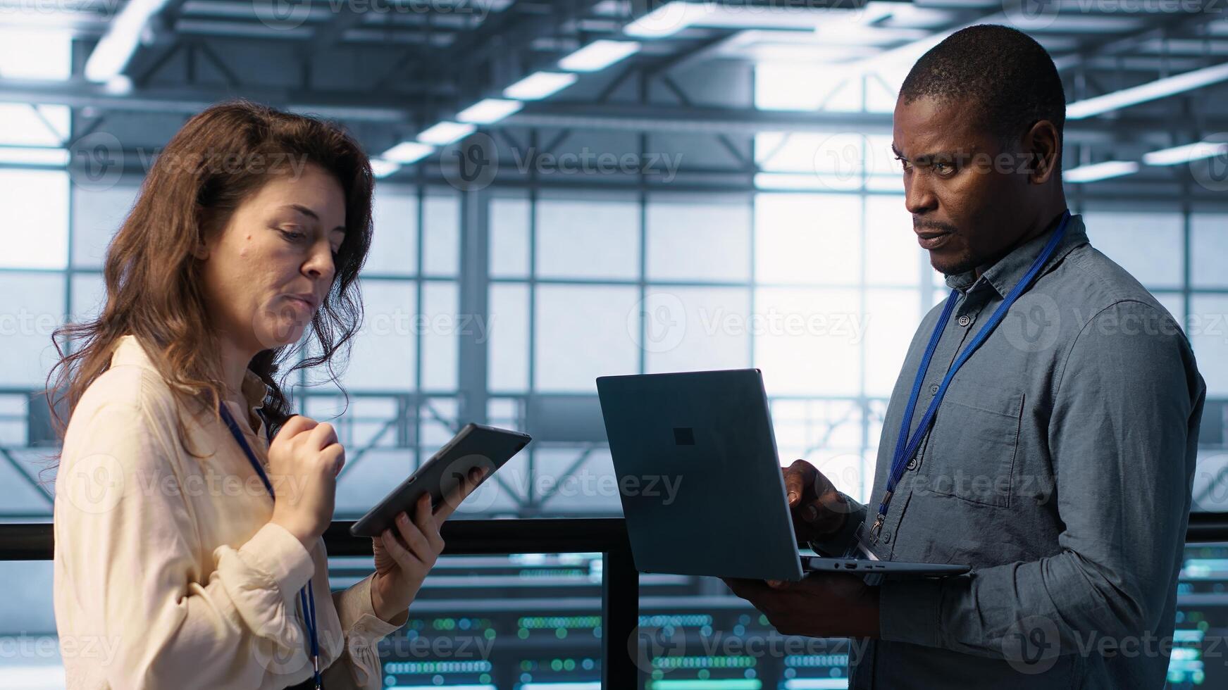 System administrators using device in data center, managing server virtualization. IT specialists using laptop in server farm, sustaining long term infrastructure reliability, camera A photo