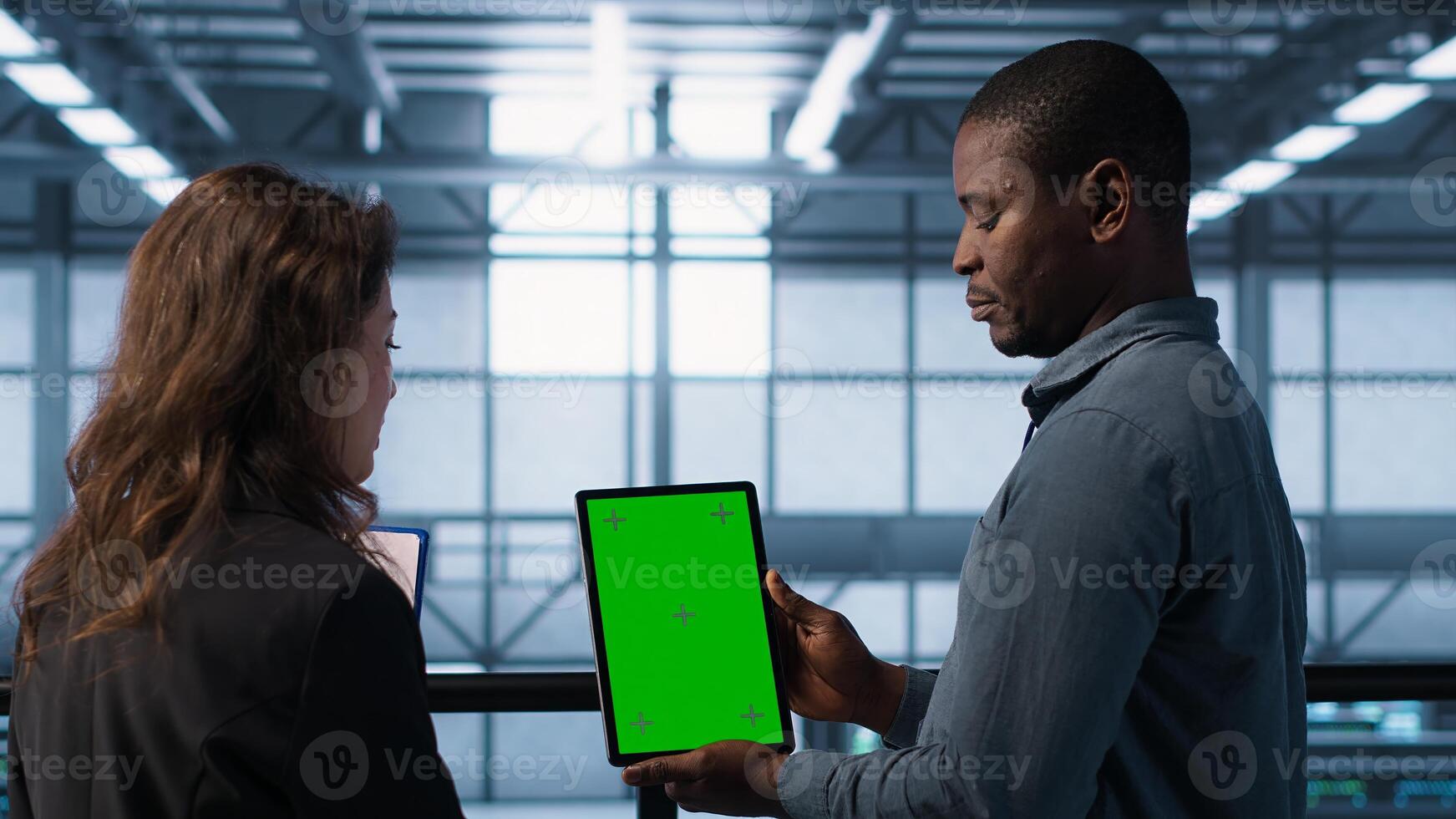 Data scientists using mockup tablet, conducting security audits to prevent bugs. African american man with colleague looking at green screen device, camera A photo