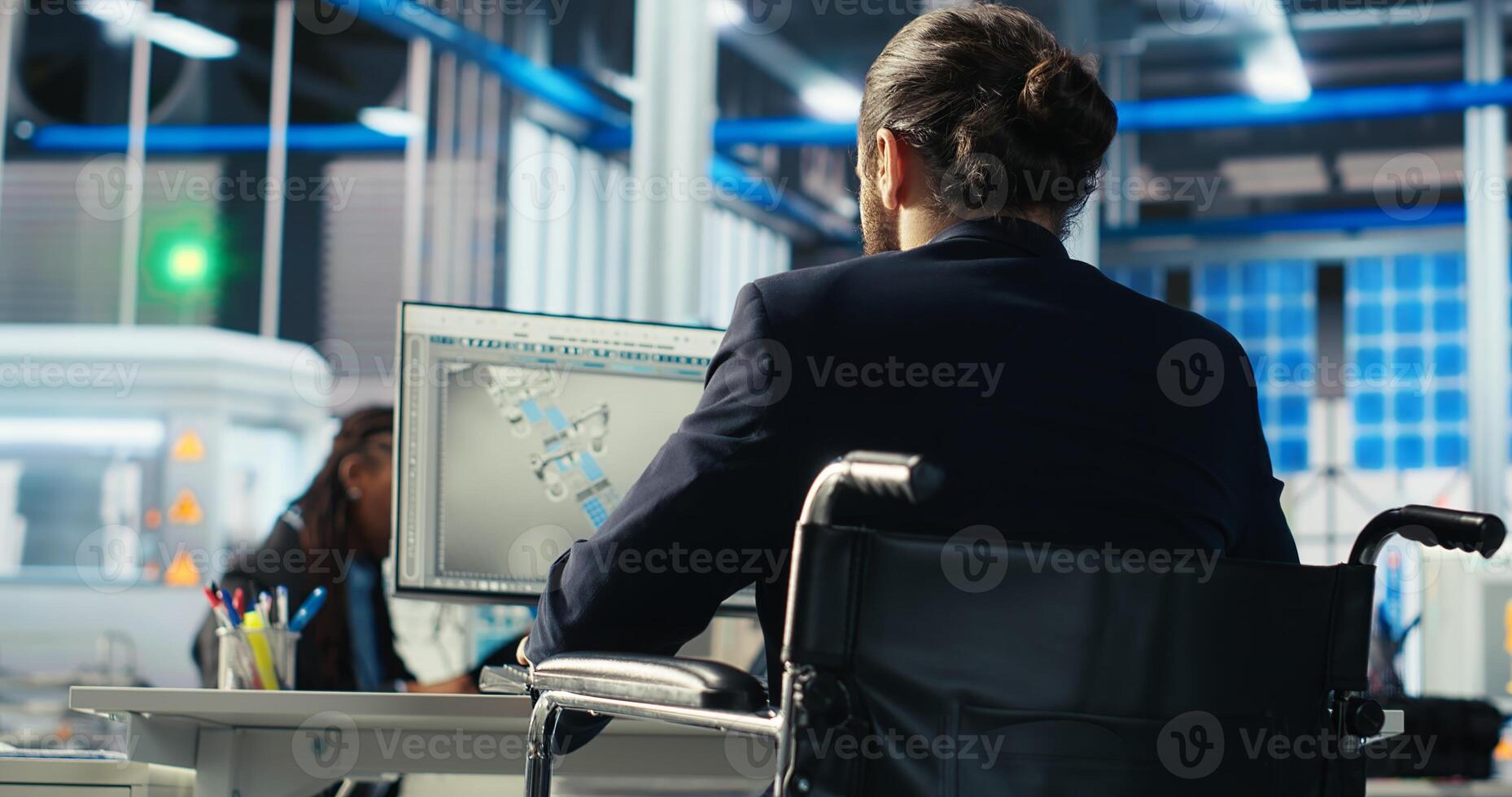 Factory worker with paraplegia in wheelchair using PC to monitor performance of solar panels manufacturing. Person with disability inspecting photovoltaics machinery on computer, camera B photo