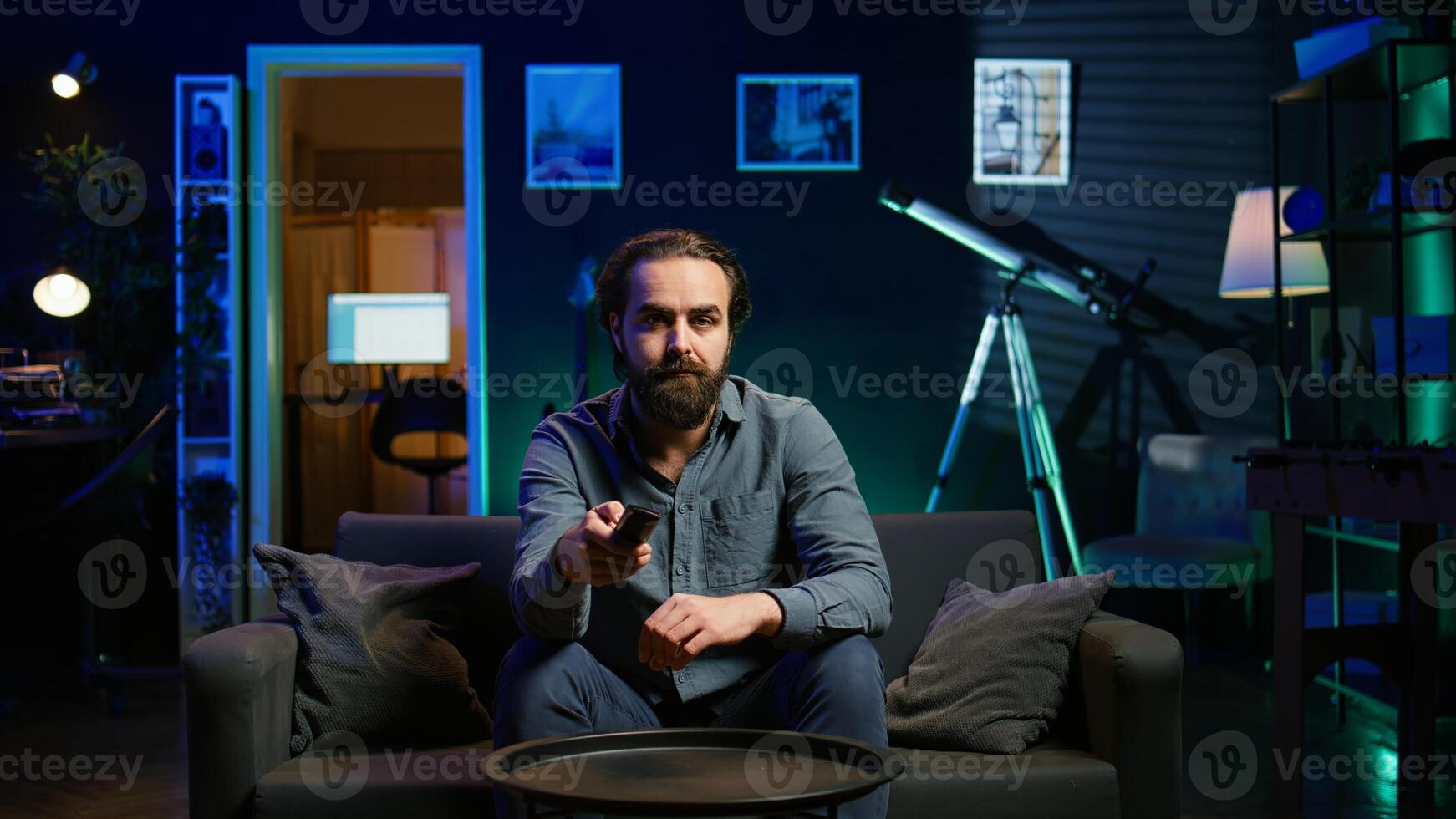 Bored person on couch in front of TV binging series on streaming services, browsing using remote. Weary man watching VOD shows on television set, zapping though channels, camera B photo