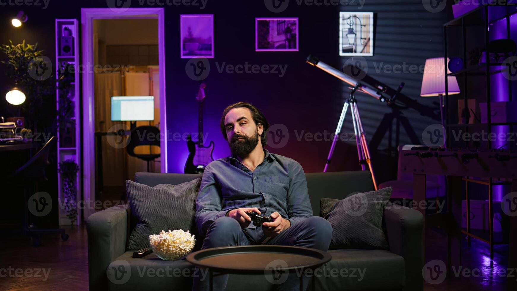 Bored gamer gaming on TV using gamepad, eating popcorn, living sedentary lifestyle. Lazy man in home theatre playing videogames and consuming snacks, sitting on couch, camera B photo