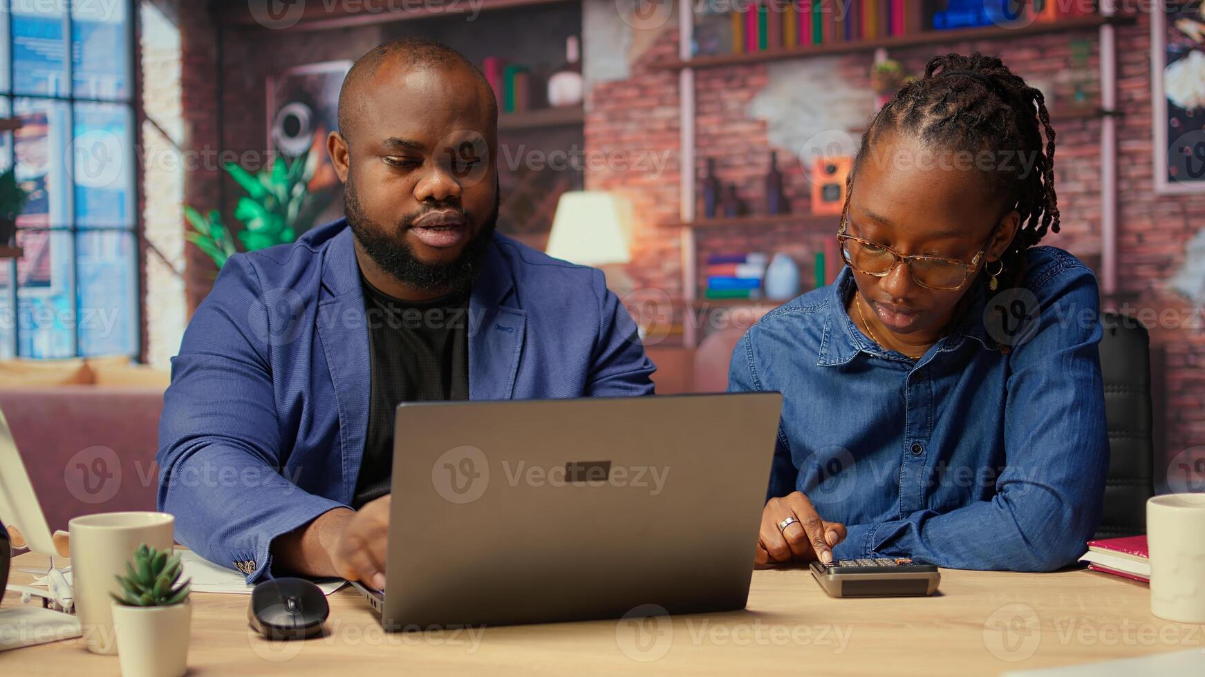 Black couple managing self employed business finances and taxes, tracking expenses and income while working remotely from loft. Doing tax calculations for debt free year. Camera A. photo