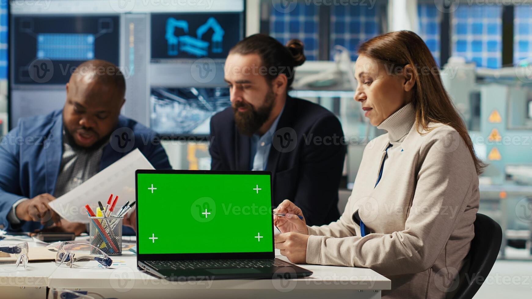 Factory engineers using green screen laptop to refine designs for increased energy output using data. Photovoltaics specialists design solar cell prototypes on chroma key notebook, camera B photo