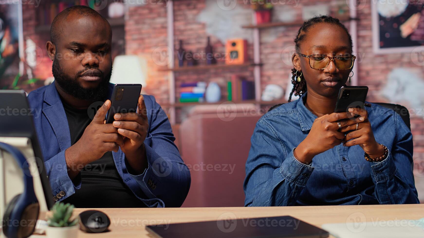 Black couple at home analyzing financial reports on mobile phones, doing teamwork to manage online freelancing tasks for productivity. Young adults achieve independence. Camera B. photo