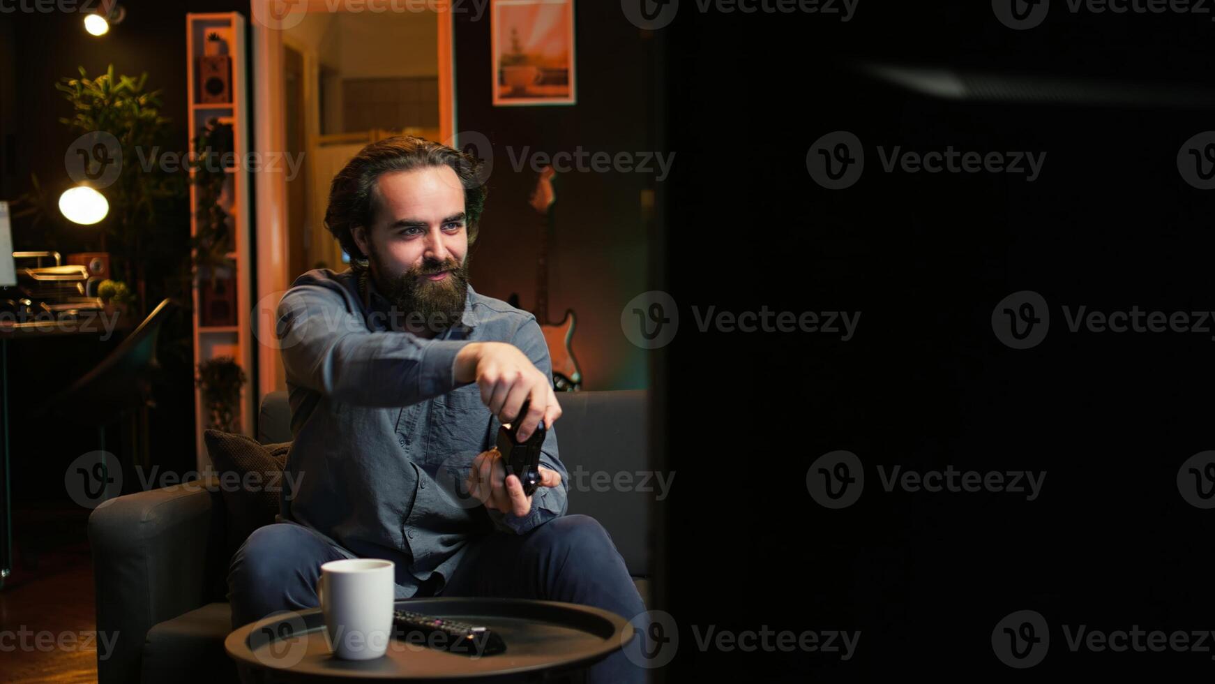 Energetic gamer excited to do gaming during leisure time. Enthusiastic man entering room, jumping on couch, excited to play videogame on console, relaxing after hard day at work, camera B photo