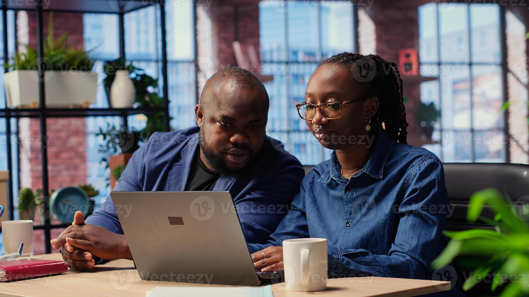 African american life partners working remotely in cozy loft, planning development strategies and discussing project ideas while using laptop to track progress. Camera B. photo