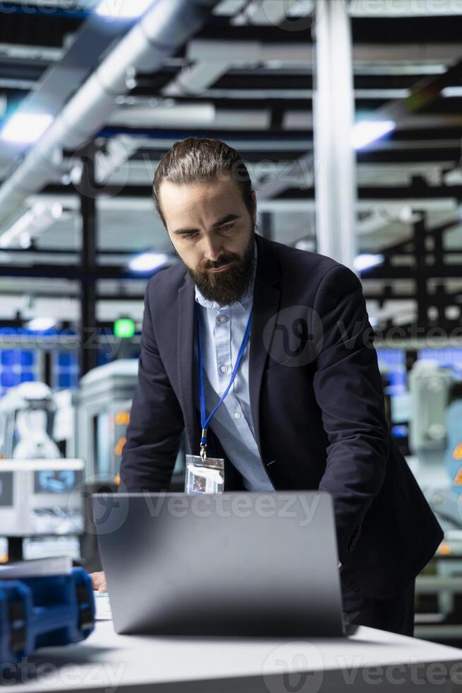 Facility supervisor in a suit monitoring solar panel production line, reflecting professional occupation and executive level involvement in renewable energy development. Solar power. photo