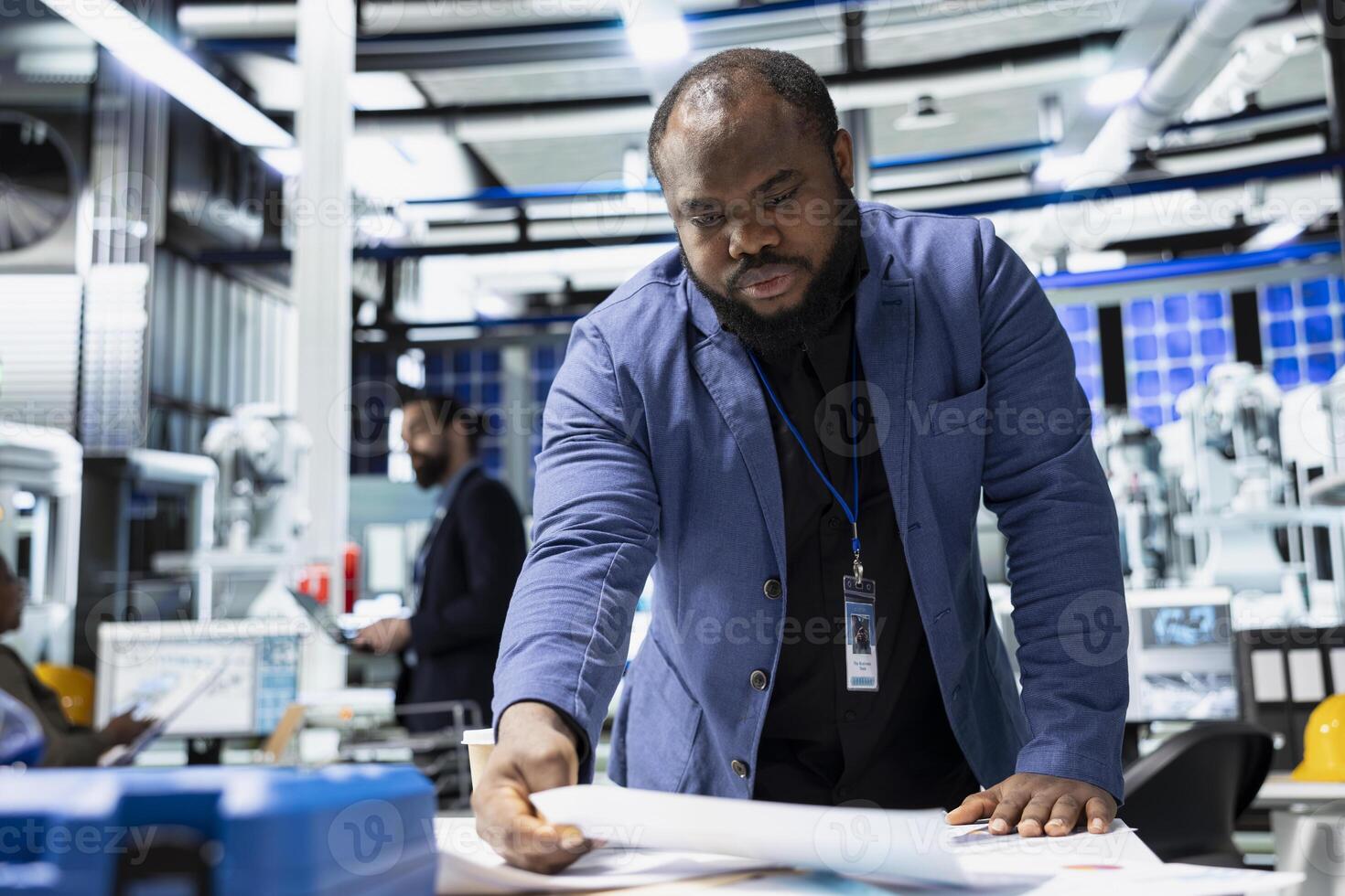 Black male sustainability consultant in suit evaluates solar panel systems and the production line in a modern factory, guiding operations toward clean energy and industrial efficiency. photo