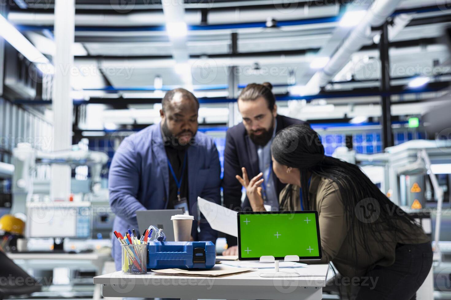 Multiethnic energy specialists coordinates activity next to chroma key, taking quality control measures in a solar tech facility. Corporate oversight and industrial execution. photo