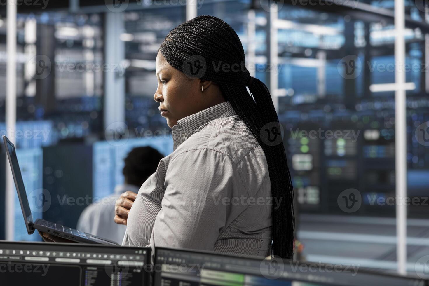 Employee using laptop to oversee data center machines providing processing resources for different workloads. Admin doing maintenance on server rigs tasked with solving complex operations photo