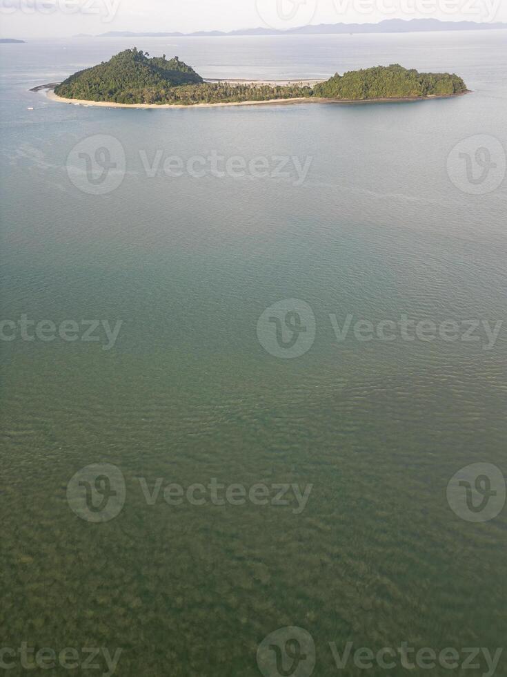Drone shot of a stunning travel destination featuring crystal clear waters and coastal cliffs, dense forest on a small island in Thailand. Sunlit seashore with sailboats on the coastline. photo