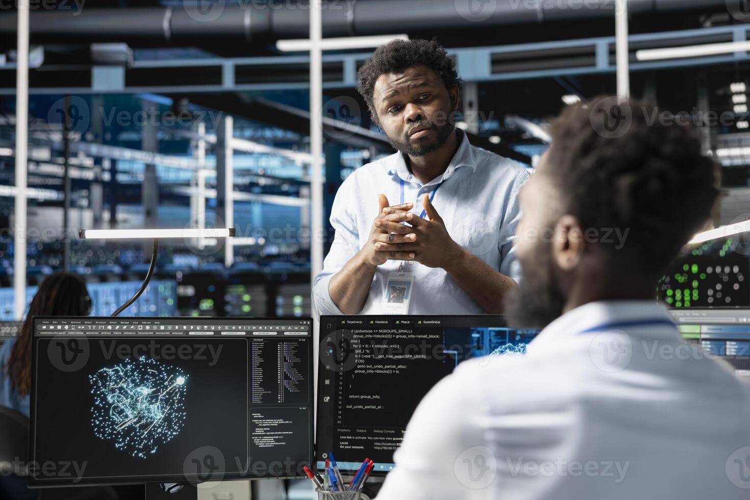 Server farm manager supervising engineer looking at data analysis graph to reduce failures. Data center team leader overseeing worker looking at AI visualization dashboard to pinpoint gear glitches photo