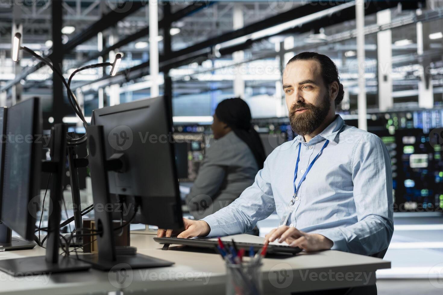 Data center programmer using PC to update servers tech, configuring gear using software tools. Server farm worker reviewing hardware analytics, ensuring reliable network operations photo