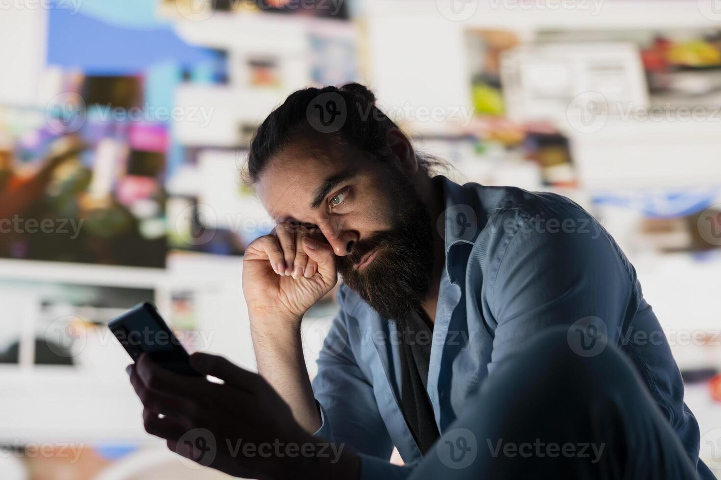 Distressed man suffers from social anxiety damage due to obsessive social media use. Young adult overwhelmed by excessive information and overload or cyberbullying affecting his self esteem. photo