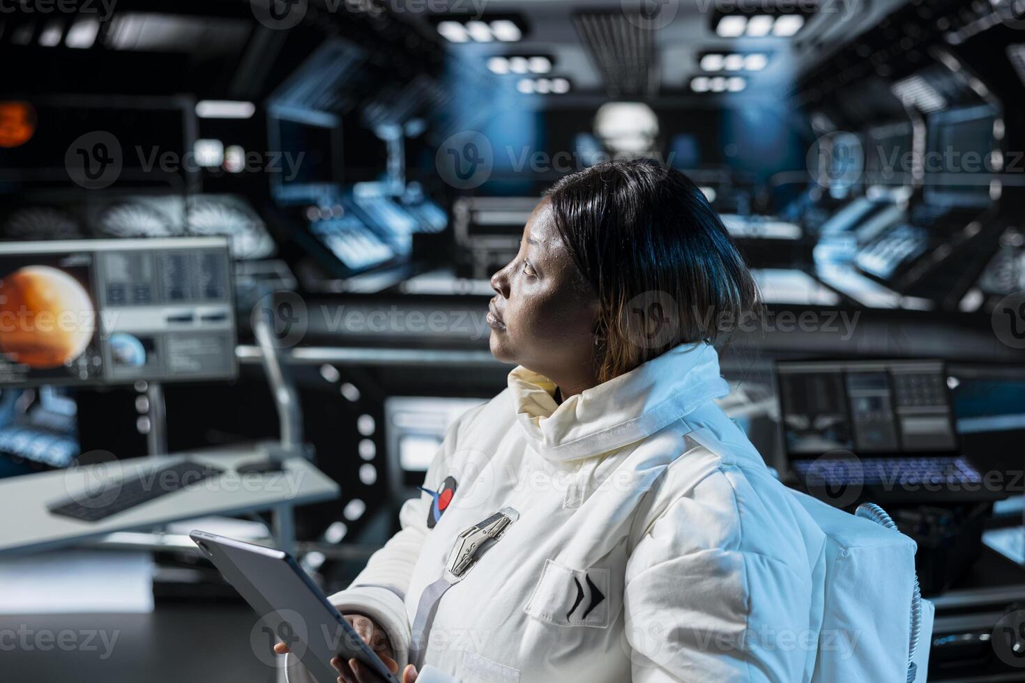 Woman in orbital station analyzing Mars planetary information on tablet. African american spaceship crew member doing Martian surface research using device to assist future planetary exploration photo