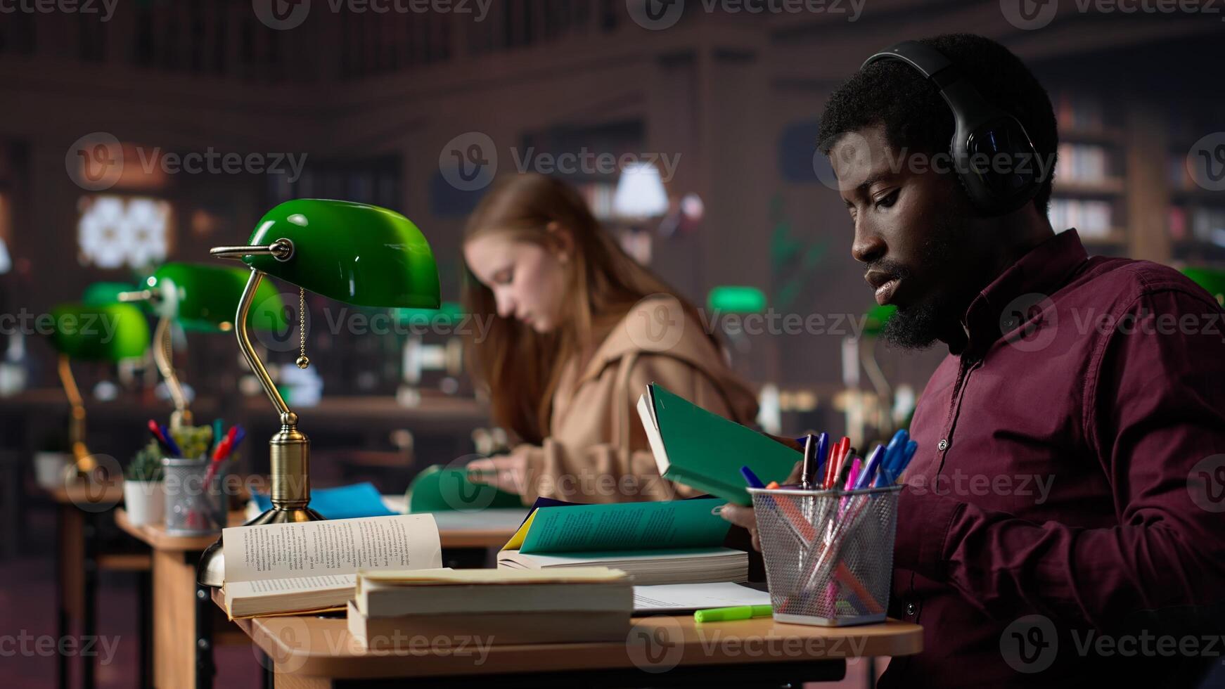 Black guy using music to help with deep focus for academic success, consulting campus university database to find reliable sources. Male college student fights for diploma. Camera A. photo