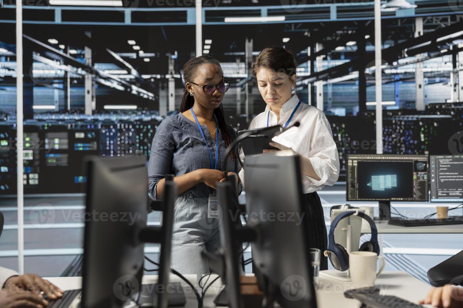 Team of technicians using tablet in server farm, analyzing data. Women working in data center examining infrastructure using device, ensuring system integrity and security photo