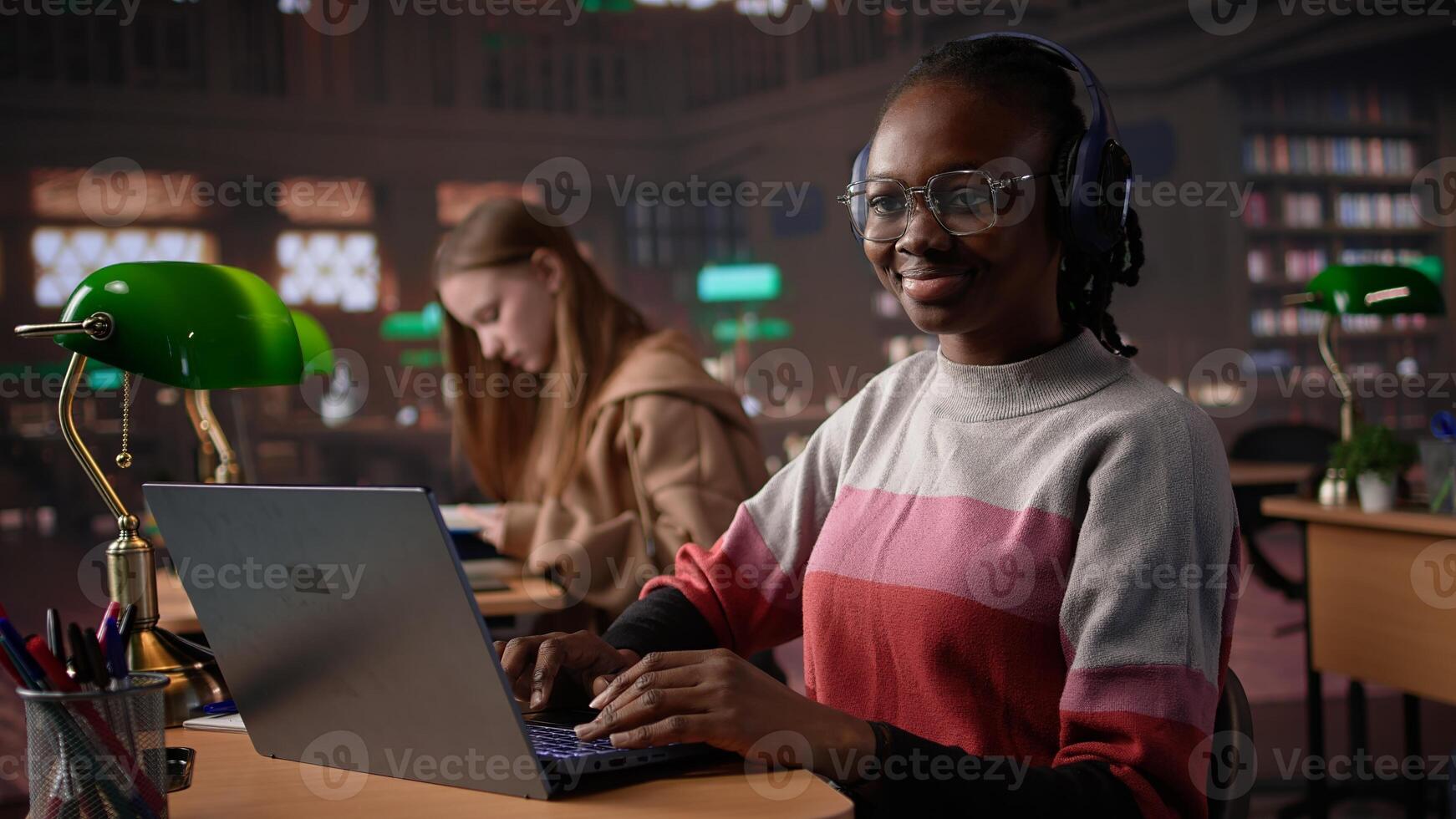 African american girl comparing course notes with data from library collection, using laptop to focus on literature assignment. Young student working on diploma project. Camera B. photo