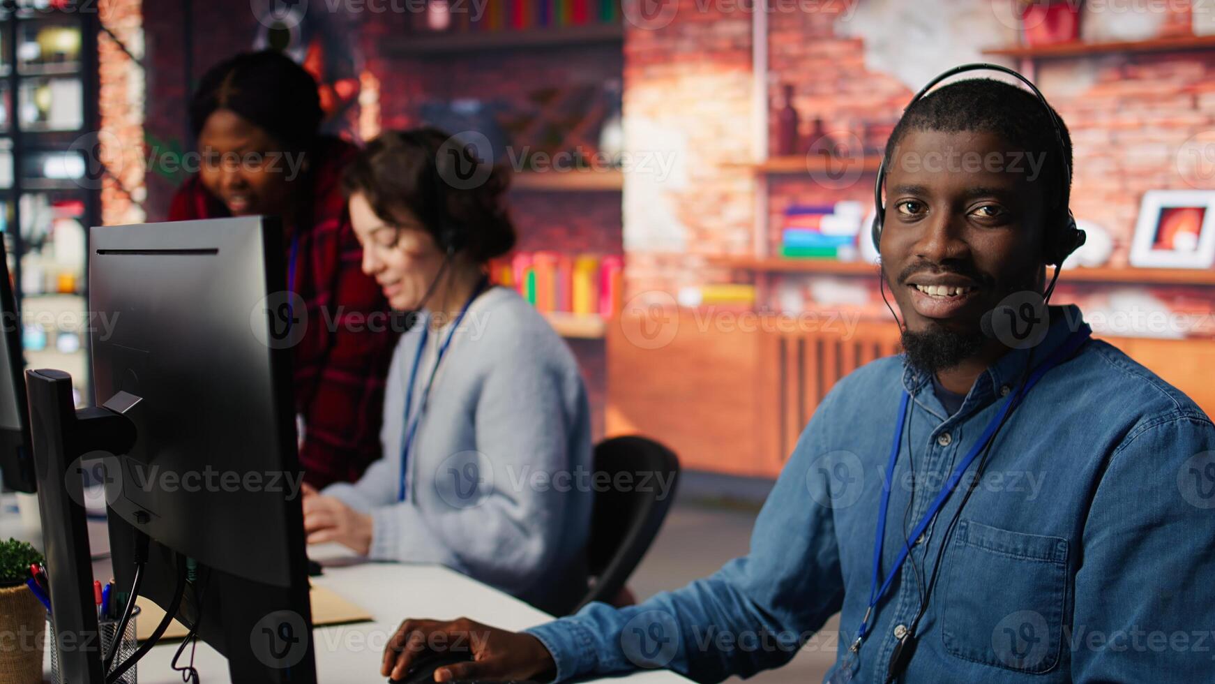 Smiling call center agent speaking with unhappy customers, using audio headset at office desk. Customer support worker handling clients complaints in company workspace, camera B photo