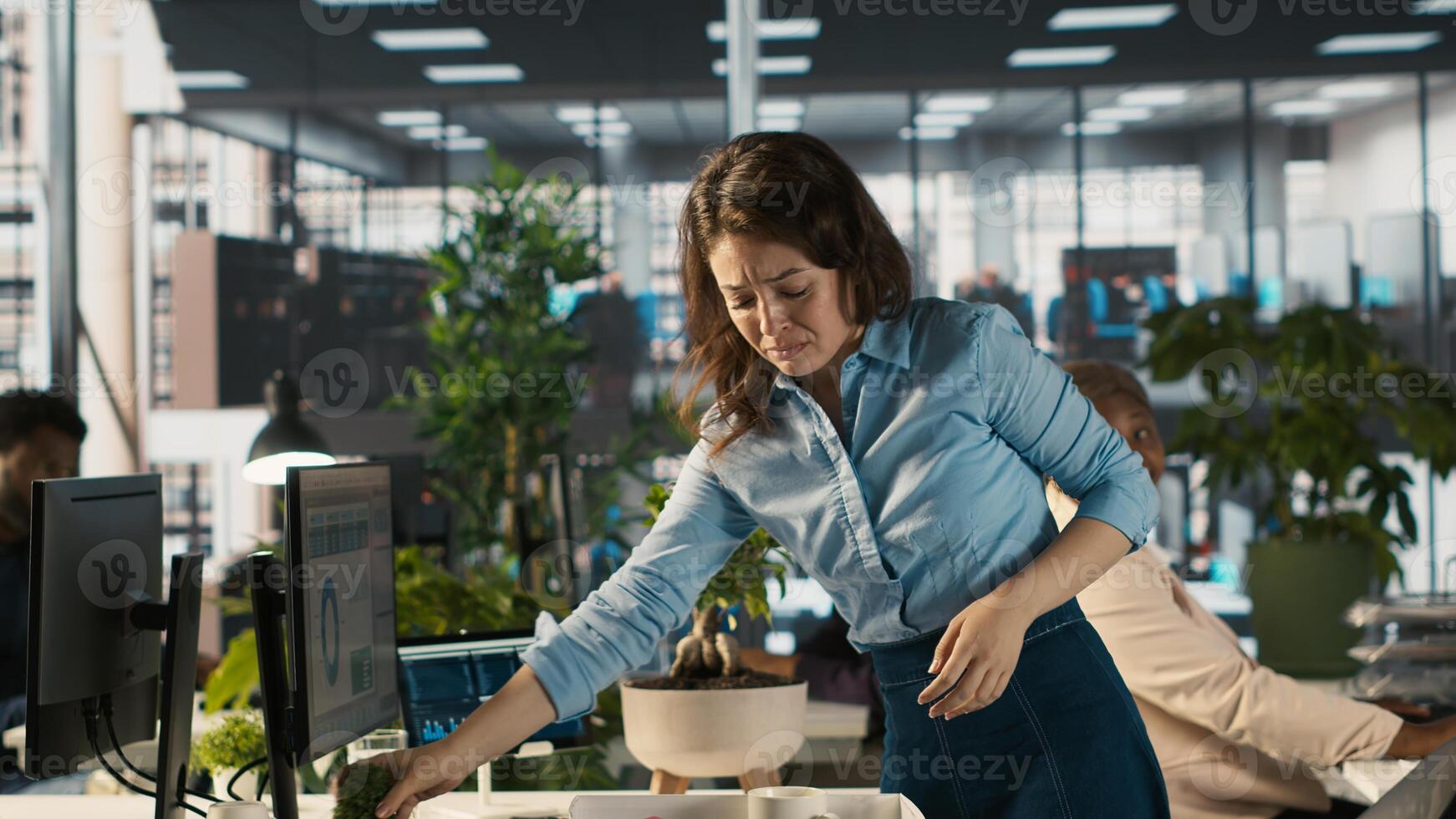 Upset worker in office packing desk plants on last day at work after quitting, saying goodbye to colleague. Employee getting fired from job during layoffs, camera A photo