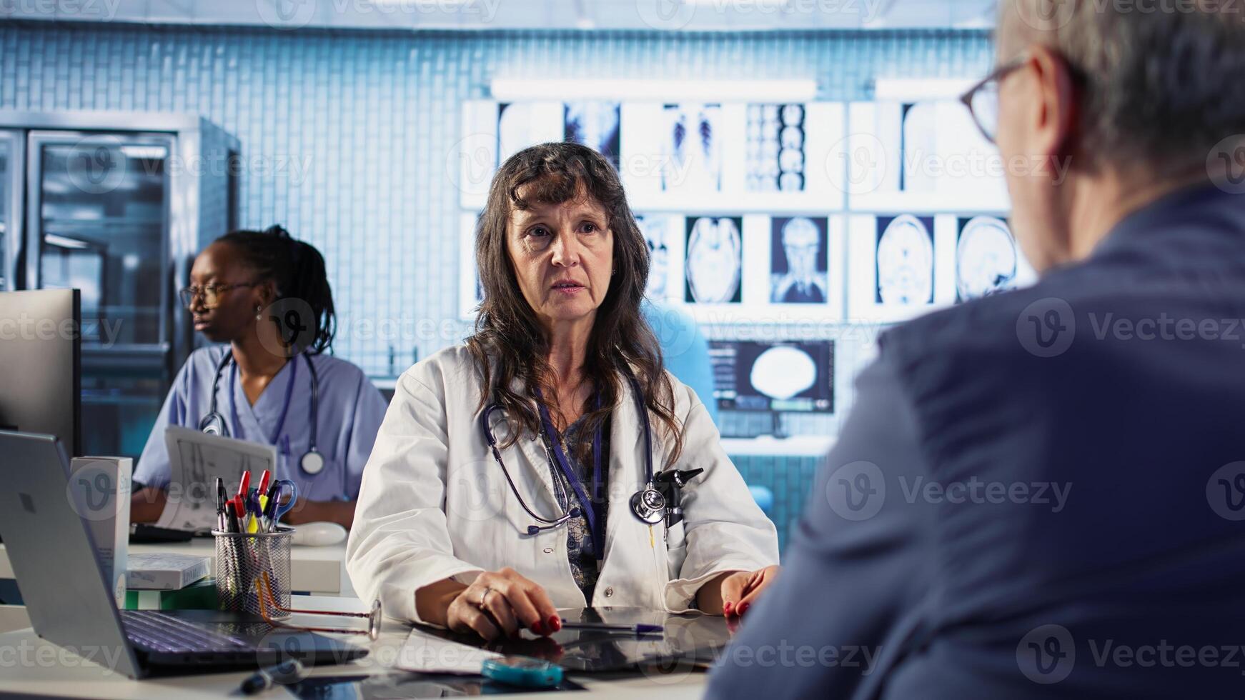 Female general practitioner giving bad worrying news to elderly man, reading x ray results and finding dangerous diagnosis. Scan interpretation for concerned senior patient. Camera A. photo