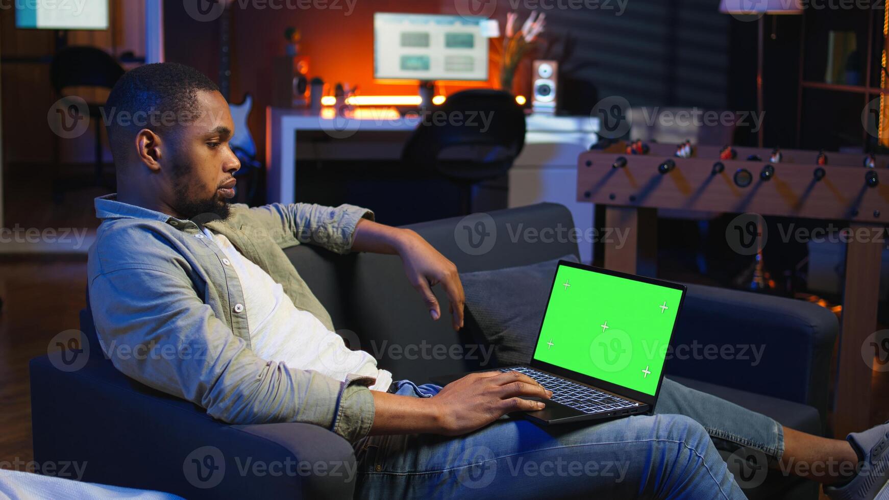 Confident young freelancer using isolated copy space in the living room, laying on his sofa in a modern living room decorated with neon lights and trendy furniture. Guy with gadgets. Camera A. photo