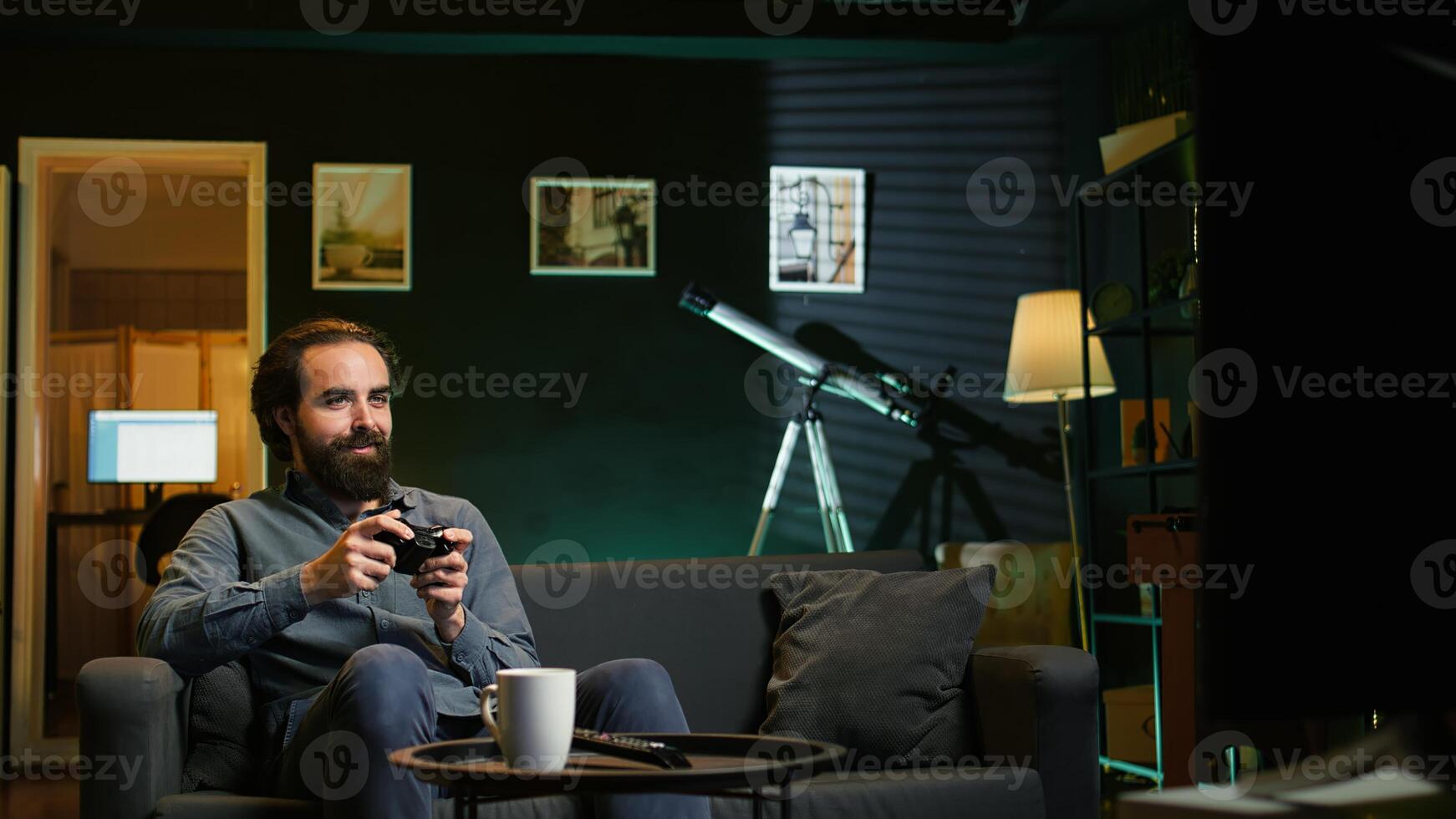 Joyful gamer at home gaming and enjoying leisure time. Smiling man sitting on couch in living room, excited to play videogame on console, relaxing after hard day at work, camera B photo