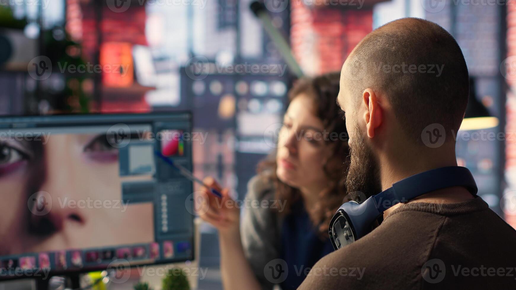 Graphic designer and photographer collaborate in studio, using photo editing software and tools on PC. Team does retouching with advanced image adjustment tools. Camera B.