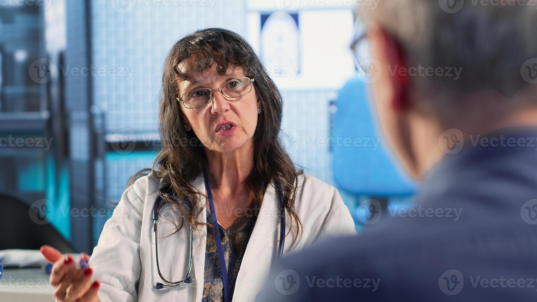 Senior woman evaluating diagnostic results with medic in cabinet, using advanced tech tools to give correct results to his patient. Care management within medical industry. Camera B. photo