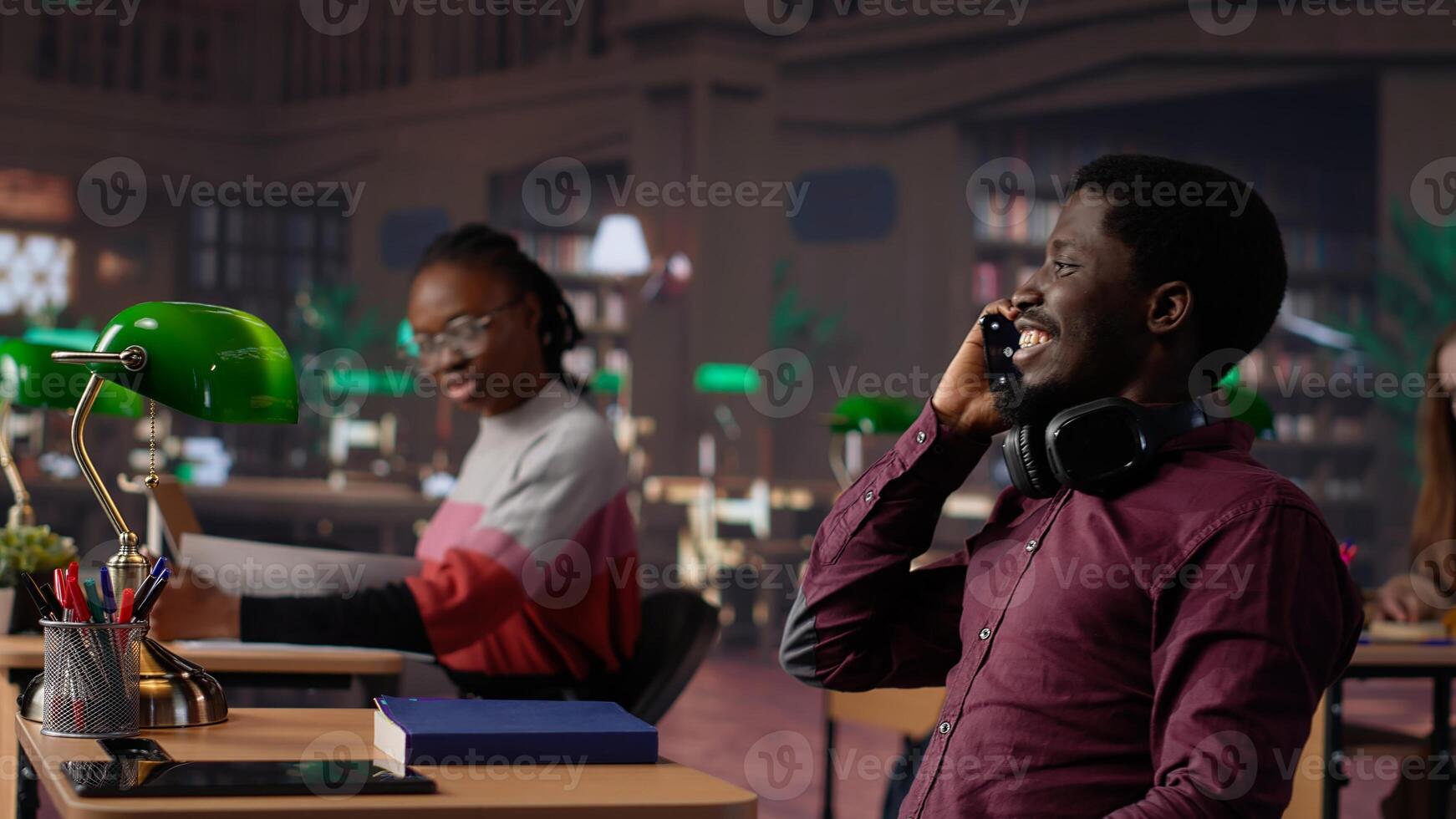 Noisy black guy disturbing pupils at library by speaking very loudly, being rude and answering phone call in study area. Disruptive annoying man asked to keep silence. Camera A. photo
