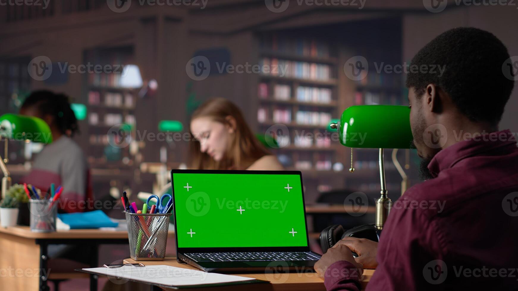 Young student working with a green screen in the university campus library, collecting academic information from verified educational sources. Pupil using research tools. Camera A. photo
