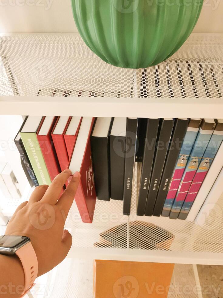 Hand reaches for a book on the shelf. Picking a right book. History, Law and Literature learning. High viewing angle. photo