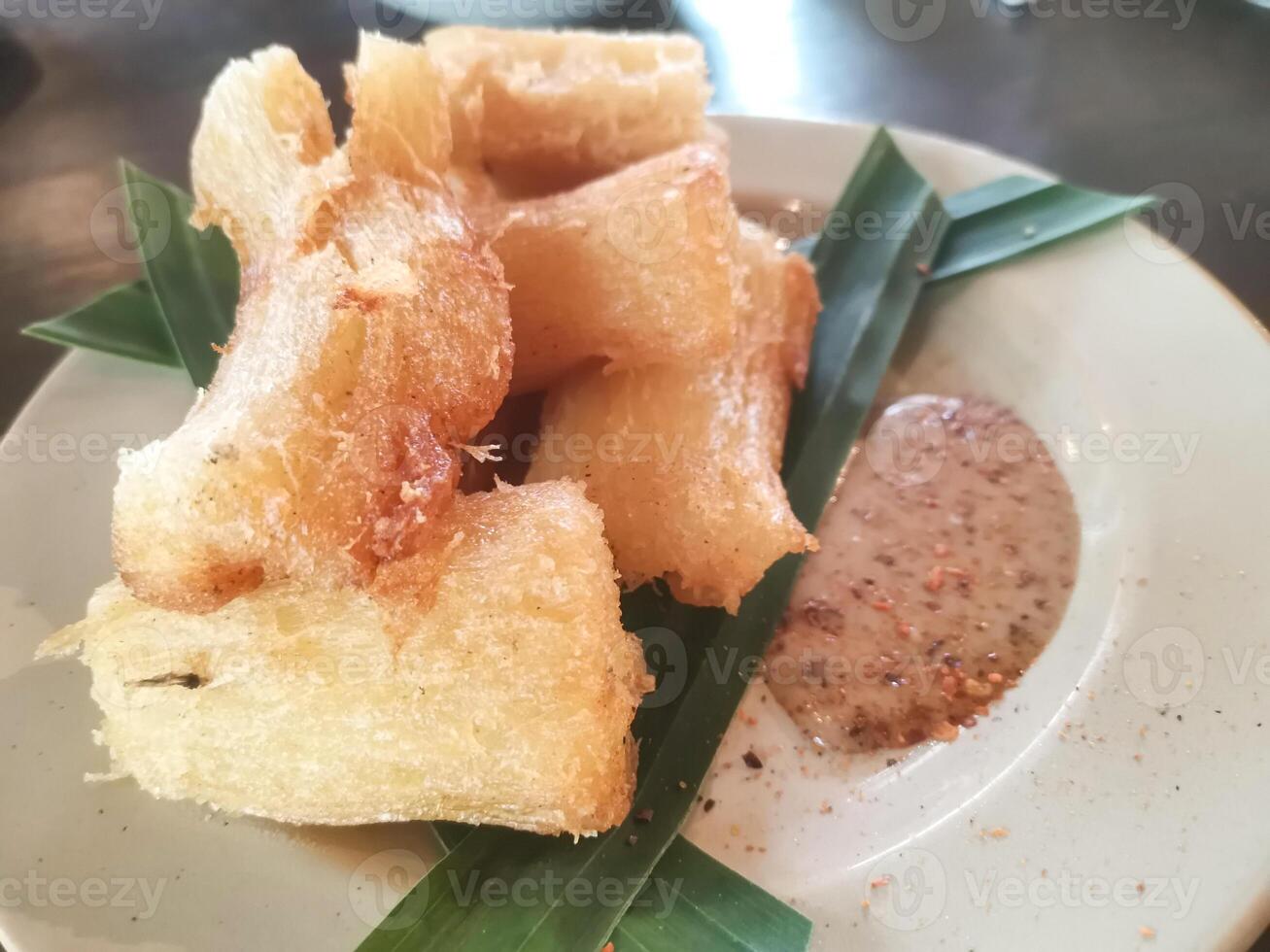 Singkong goreng or fried cassava is a traditional Indonesian food. Served on a white plate decorated with banana leaves. Eaten with sesame peanut sauce. Selected focus. photo