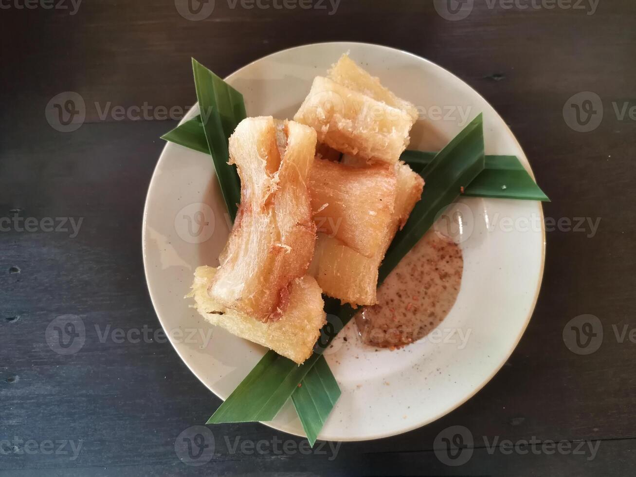 Fried cassava with brown sauce on a white plate with green leaves. Top view photo