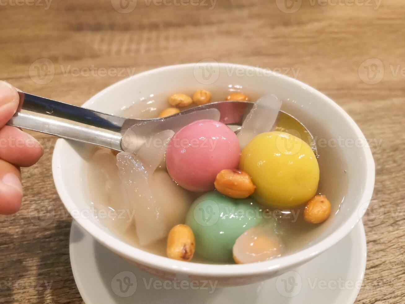 Colorful Wedang Ronde in a white bowl. Wedang ronde contains colorful sticky rice balls filled with peanuts. Served with ginger syrup, peanuts, and aren fruit. Traditional Indonesian drink. photo