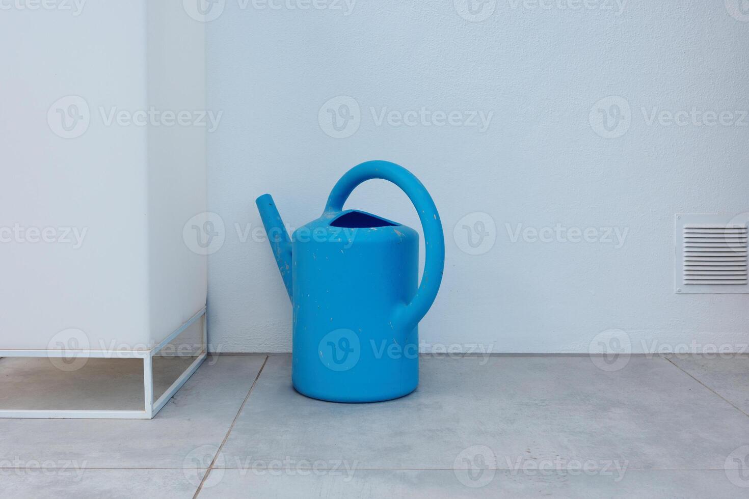 Bright blue plastic watering can on modern tiled floor on a patio. Concept of minimalism, gardening and practical household utility in contemporary spaces. photo