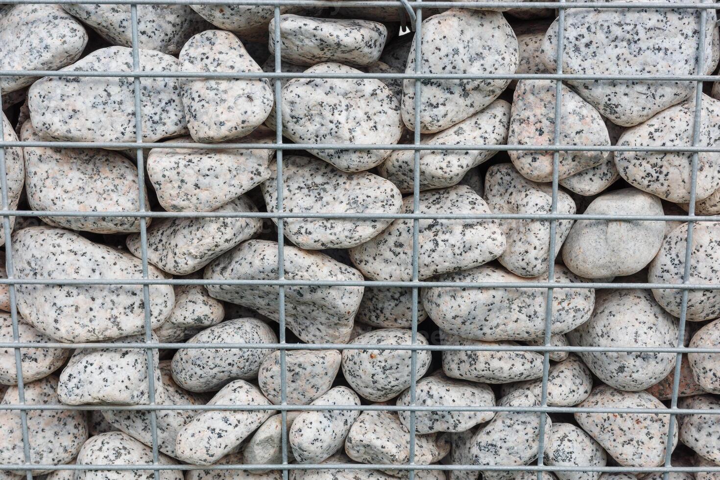 Close-up of rounded granite stones enclosed in a metal gabion cage for landscape construction. Concept of durability, architectural texture and natural stone arrangement in modern design. photo