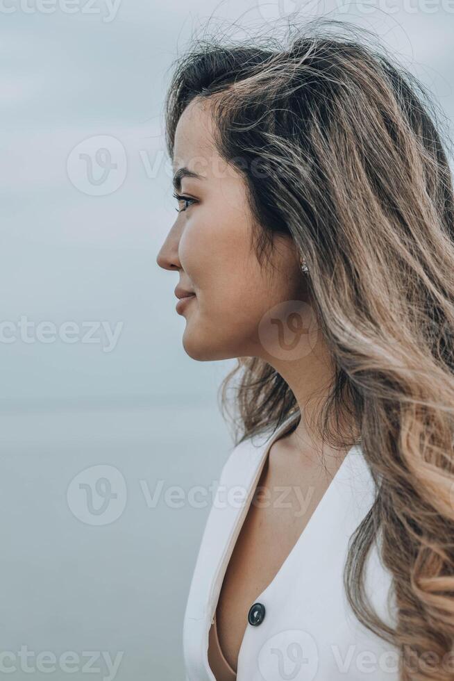 Asian woman on a calm lakeside, dressed in white outfit, displaying a confident and cheerful emotion, concept of wellness, skincare, personal development, vertical photo