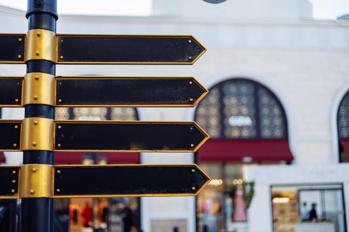 Directional signpost with blank arrows in a bustling shopping area during daytime. photo