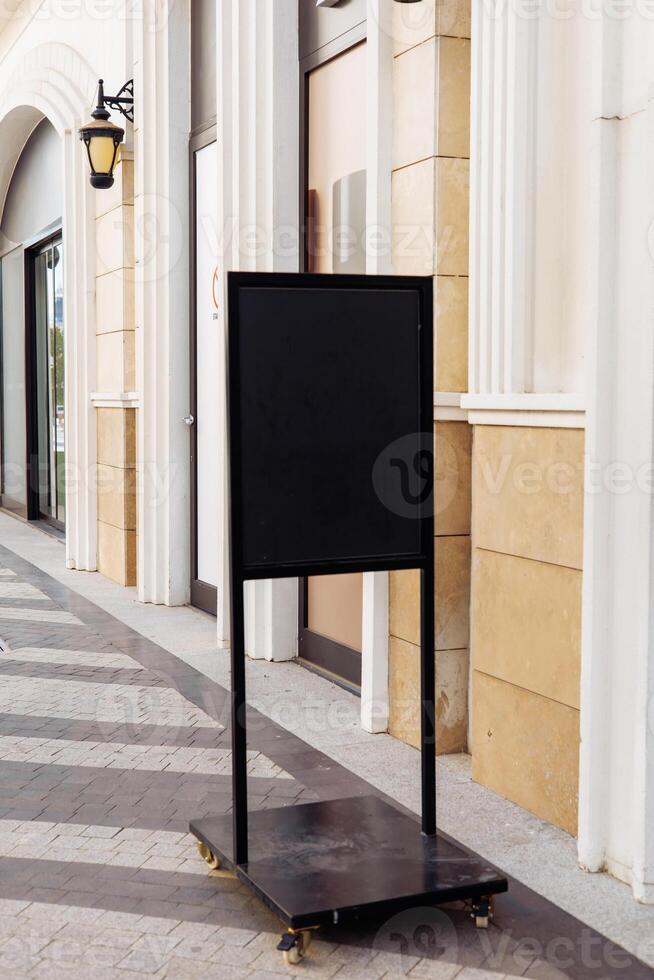 The Black sidewalk sign stand placed on a city street near shops and palm trees photo