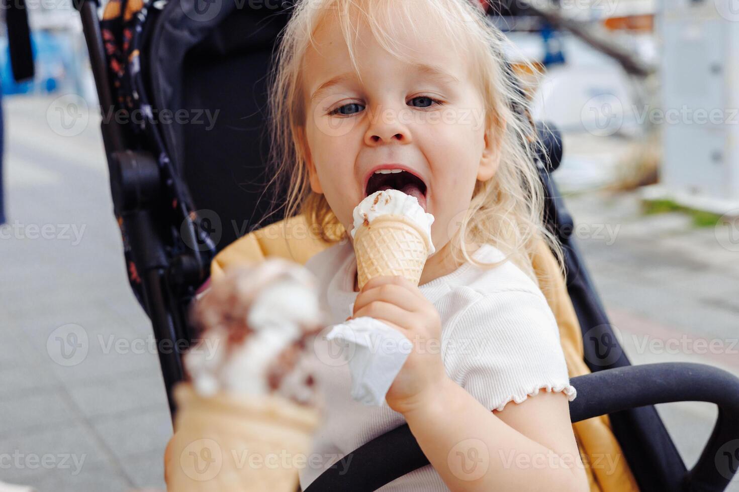 Toddler girl enjoys ice cream while exploring the marina during summer trip with her family photo