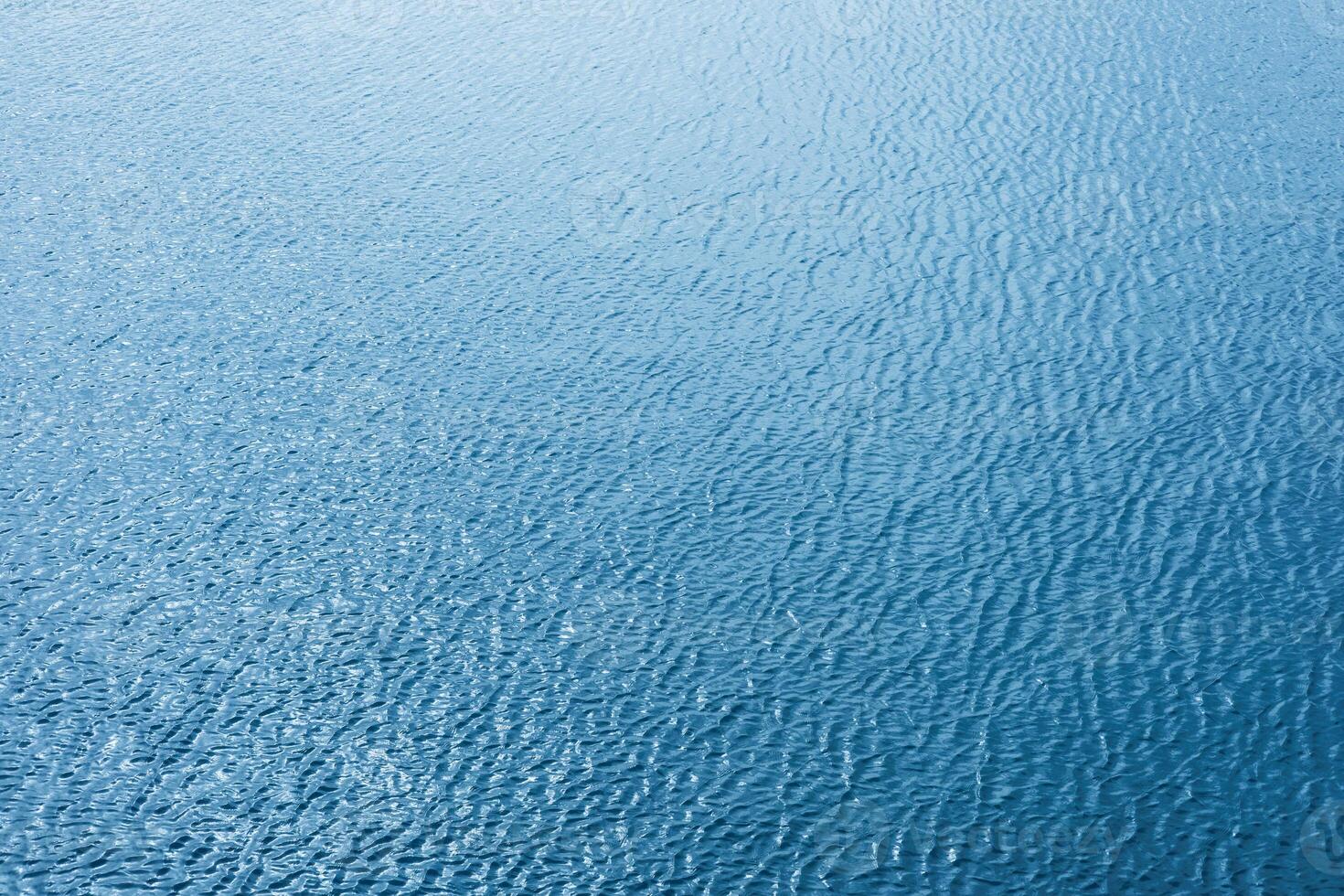 Tranquil blue water surface reflecting sunlight against soft ripples. photo