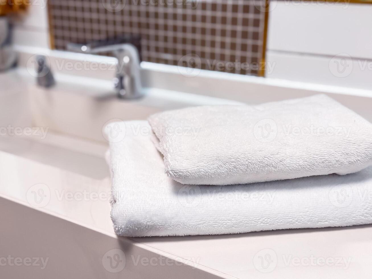 Soft white towels neatly stacked on a clean countertop in a modern bathroom setting. photo