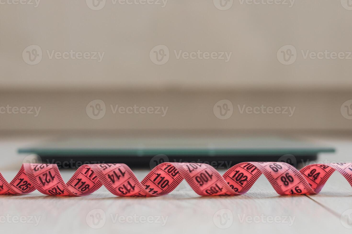 close-up of pink measuring tape with a digital scale in the background. The scene emphasizes health and fitness concepts. photo