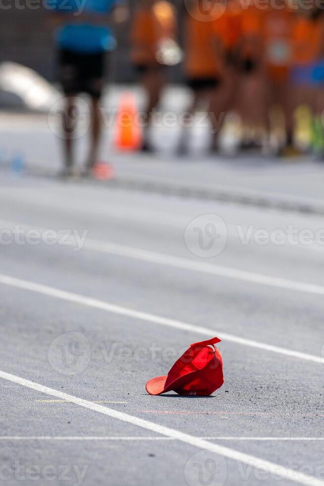Red sports cap lying on the ground of a running track with blurred athletes in the background photo