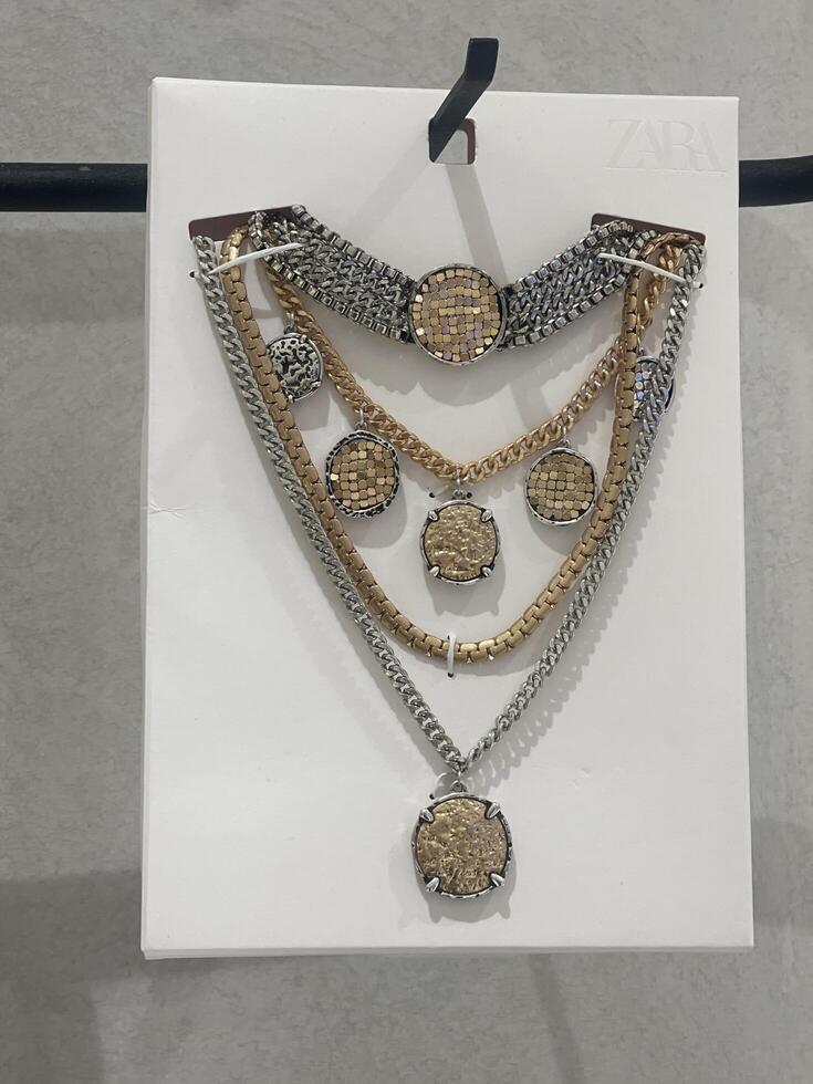 VALENCIA, SPAIN - MAY 30, 2025. Close-up of a set of metallic necklaces with coin-inspired pendants on a Zara store display card. Fashion jewelry sold in a Spanish retail clothing store. photo