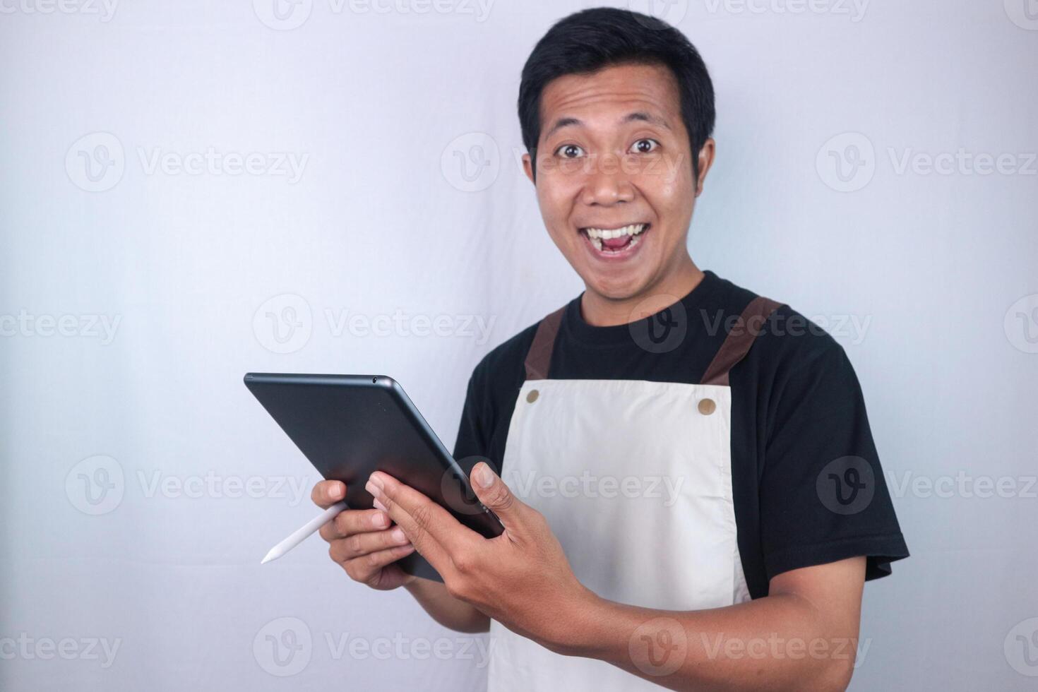 Young smiling man barista barman employee wear apron work in coffee shop hold use tablet photo