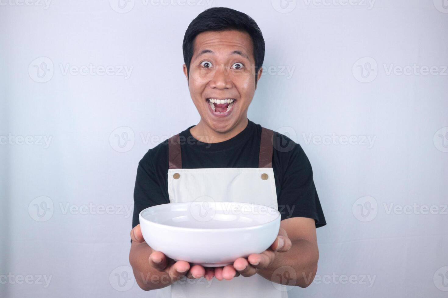 Funny excited face expression asian man chef or waiter shows empty white bowl, presenting something. photo