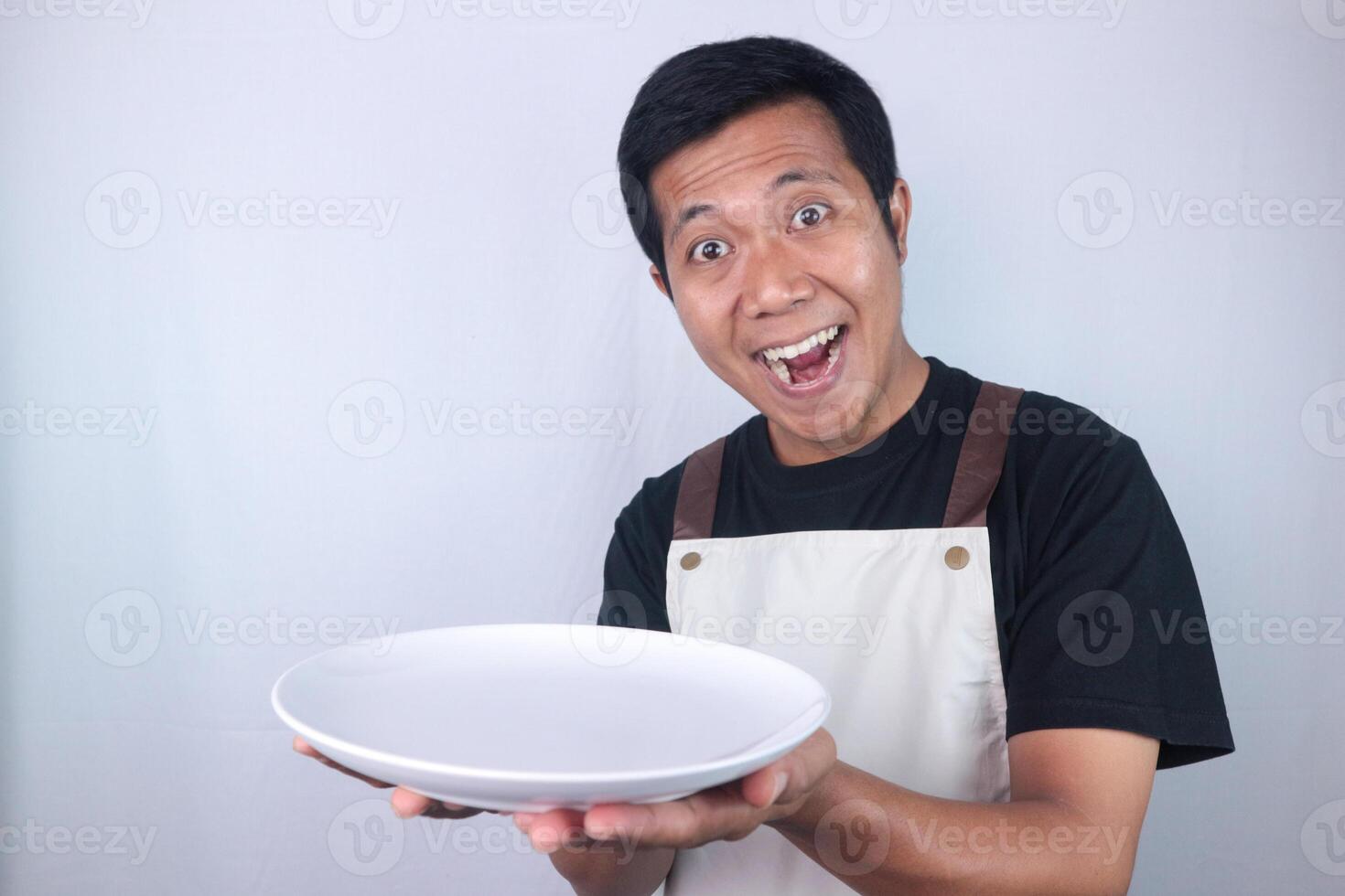 Funny expression asian man chef or waiter shows empty white plate, presenting something photo